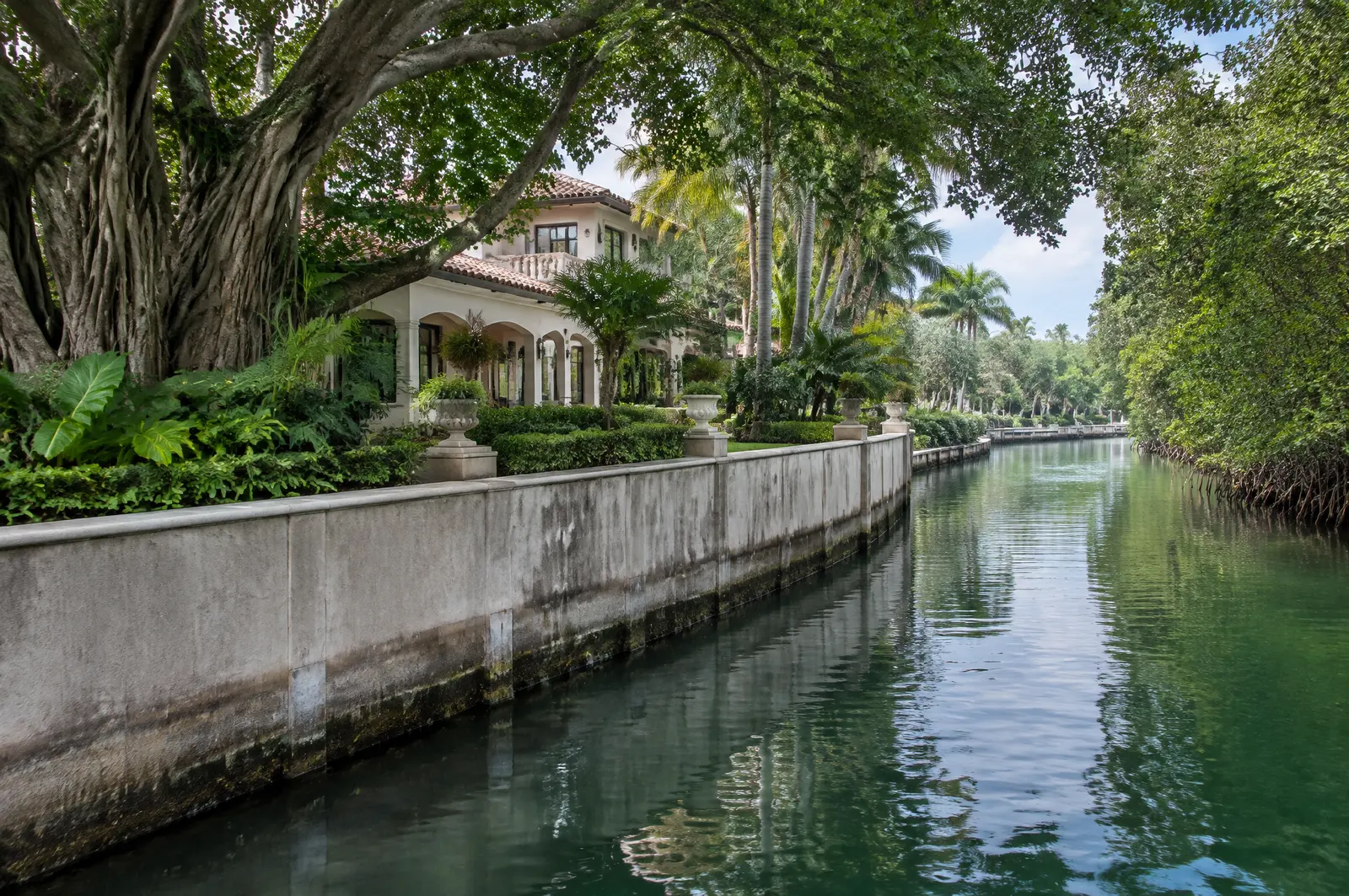 Tall seawall on a winding mangrove-lined waterway below a Mediterranean revival home