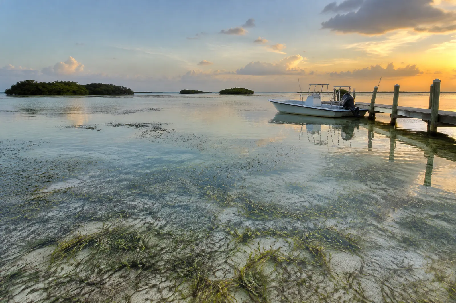 Shallow clear Florida Bay flats with seagrass and pale sand, a small boat at a short dock and mangrove islets
