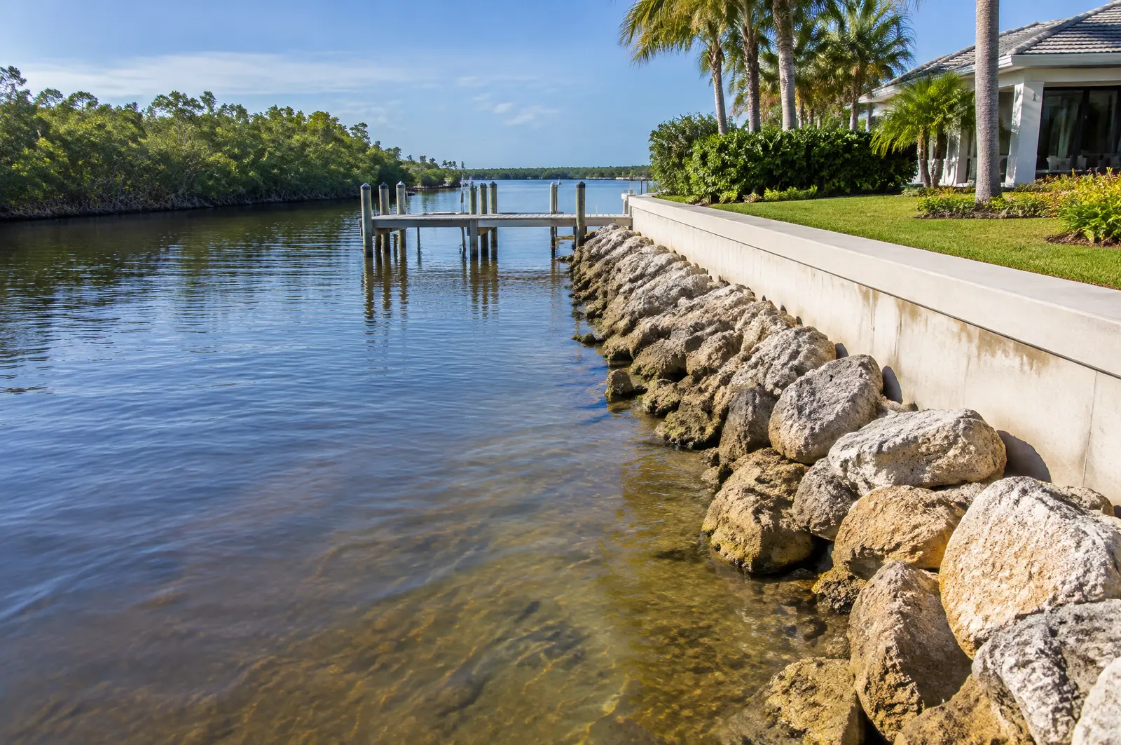 Residential seawall with limestone riprap at its toe on a calm tidal river with mangroves upstream