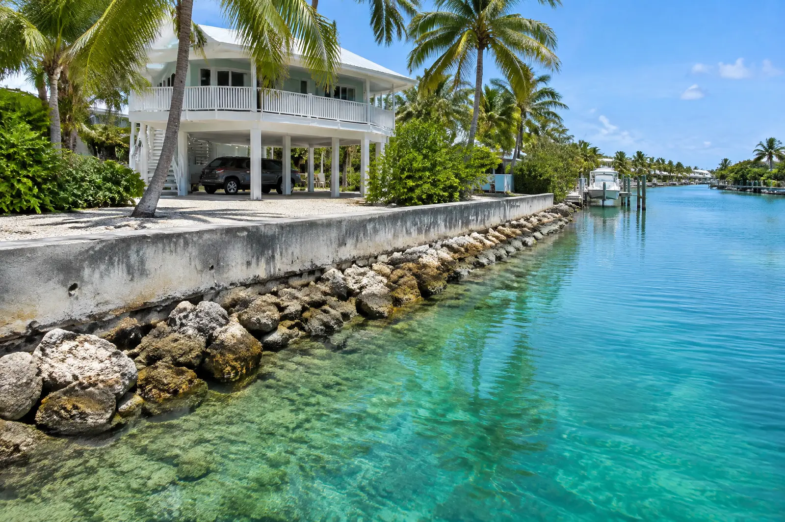 Weathered seawall with riprap at its toe on a clear Keys canal below a stilt home