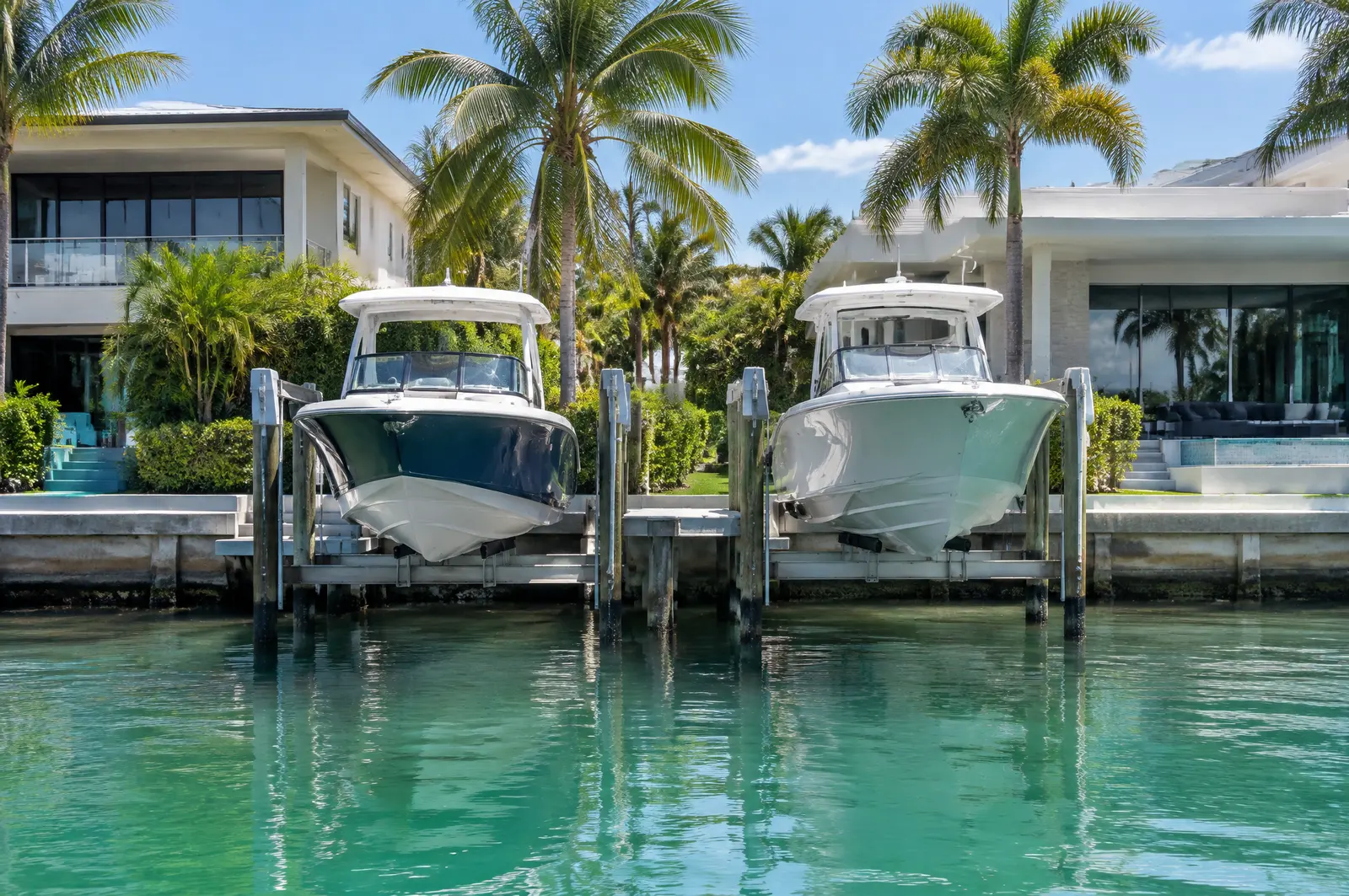 Two boats on four-post lifts behind modern homes on a narrow canal with clean seawall caps