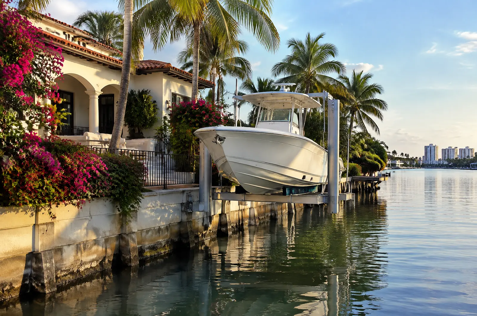 Boat raised on a seawall-mounted elevator lift at a canal home with palms and bougainvillea