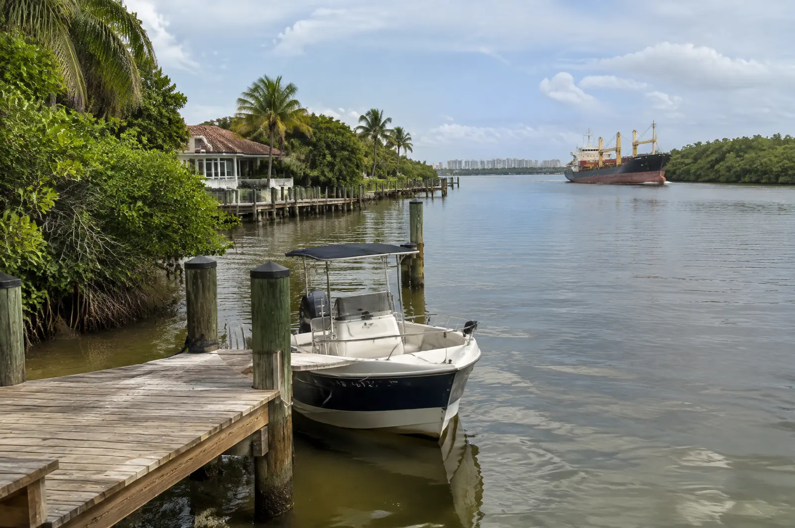 Private timber dock with a small boat on a calm river lined with mangroves and older waterfront homes