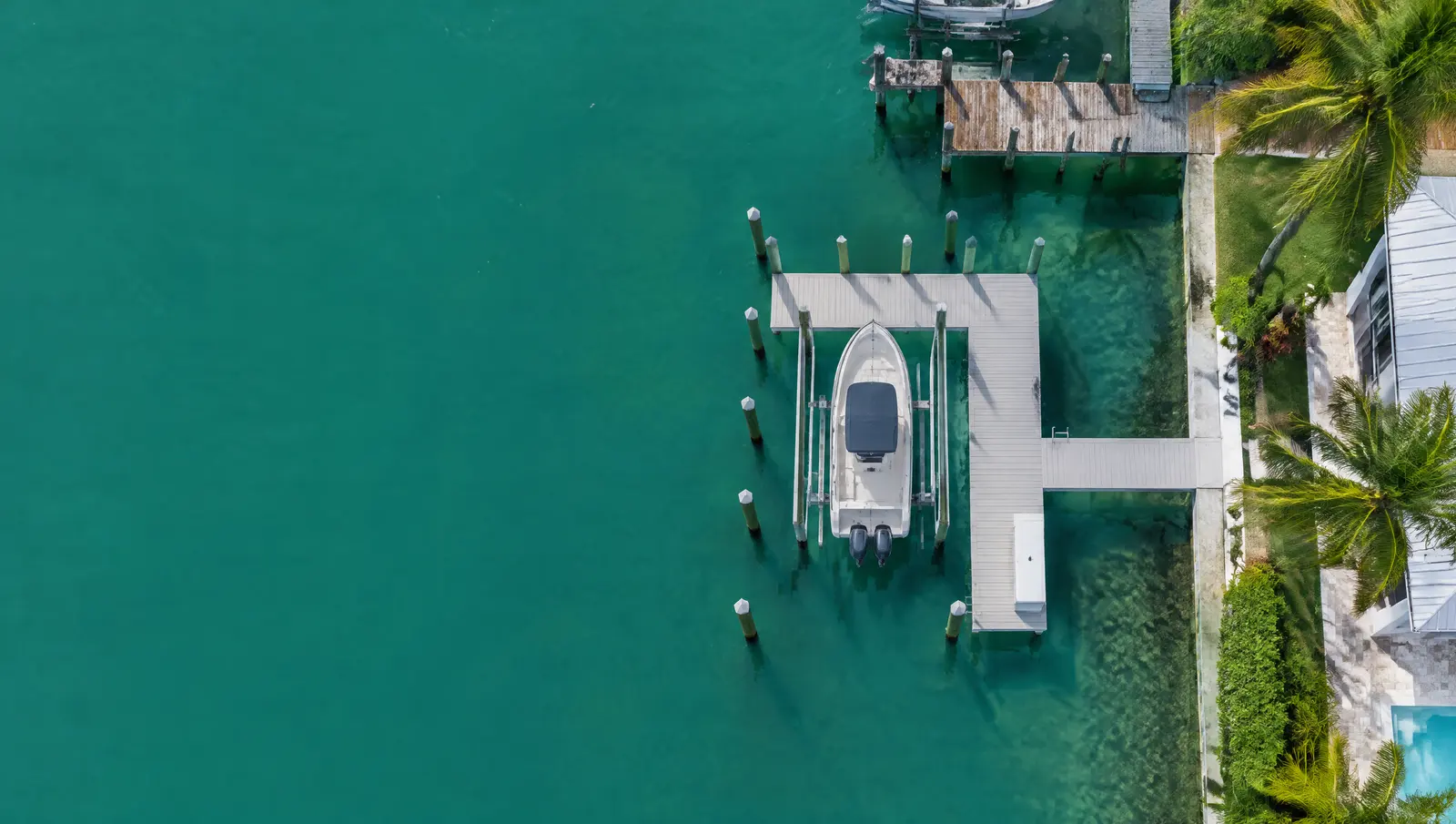 Overhead view of a new composite dock with a boat lift beside older docks on a turquoise canal