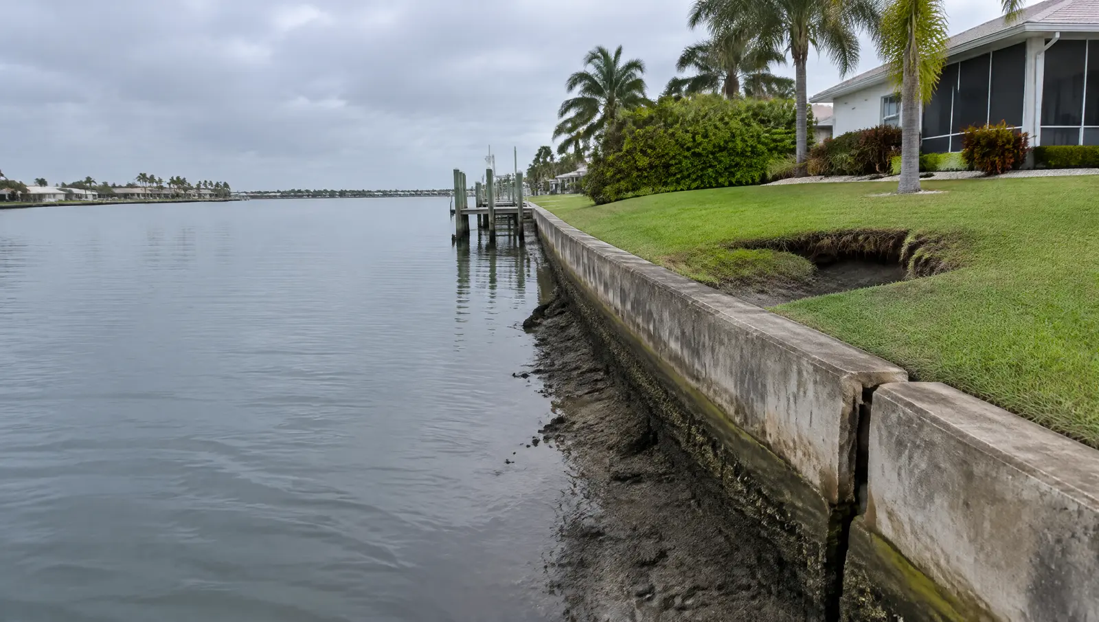 Small sinkhole in a lawn behind an old seawall with a visible gap at a wall joint