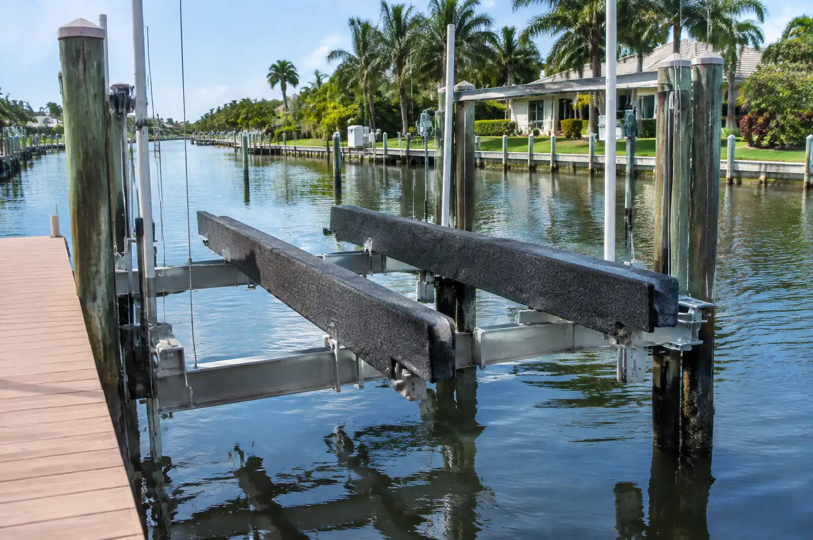 Empty boat lift cradle with carpeted bunks raised above calm canal water beside a dock