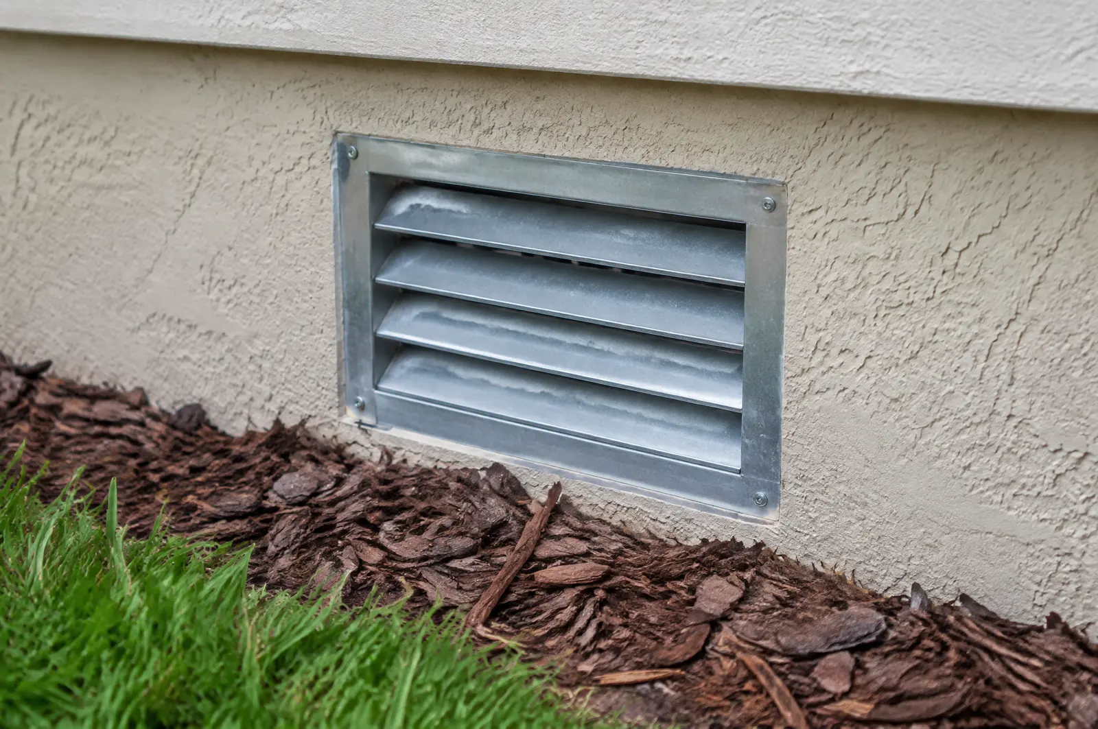 Louvred metal flood vent set low in a stucco foundation wall