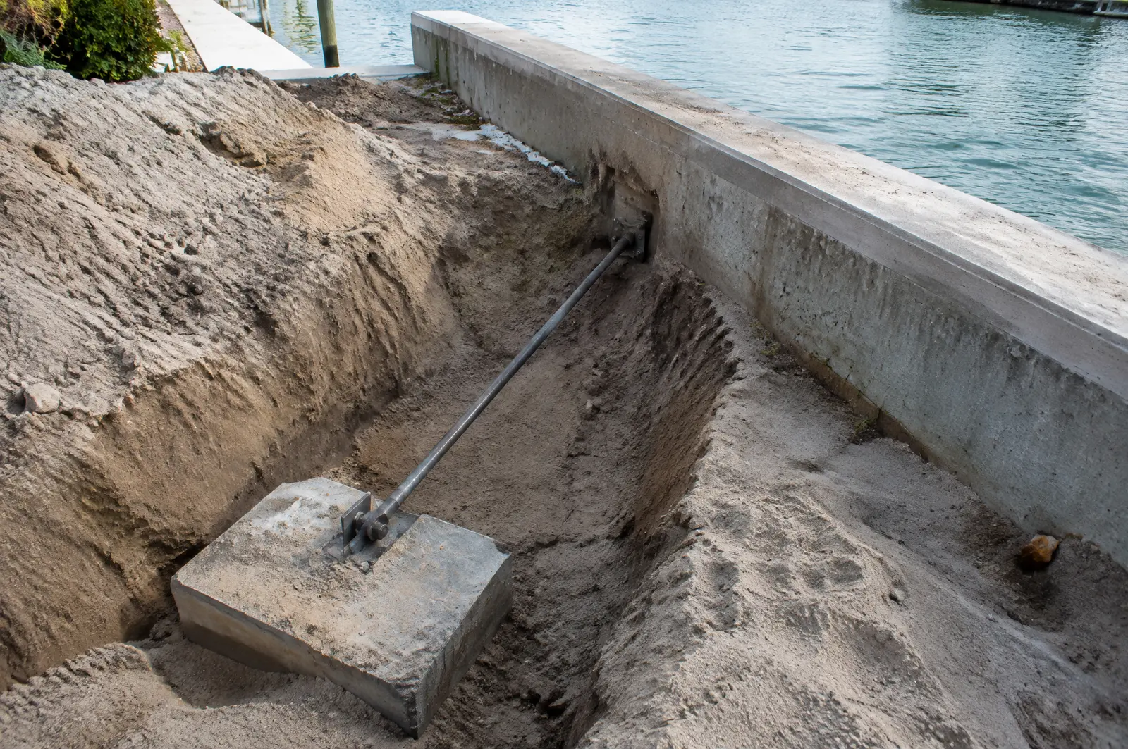 Trench behind a seawall exposing a steel tie rod running back to a concrete anchor